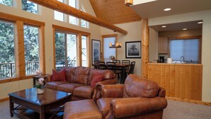 A spacious living area with a large L-shaped leather sofa, a coffee table, and a dining table with chairs. There are large windows providing natural light and a view of the outdoors. - Running Y Resort (Klamath Falls)