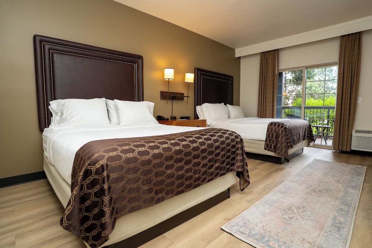 A hotel room with two beds, a large window, and a view of the outdoors.