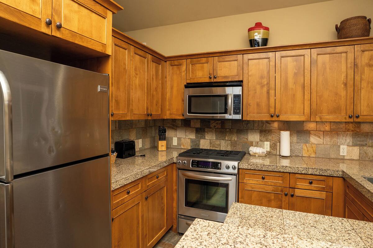 A kitchen with wooden cabinets, stainless steel appliances, granite countertops, and a stone backsplash.