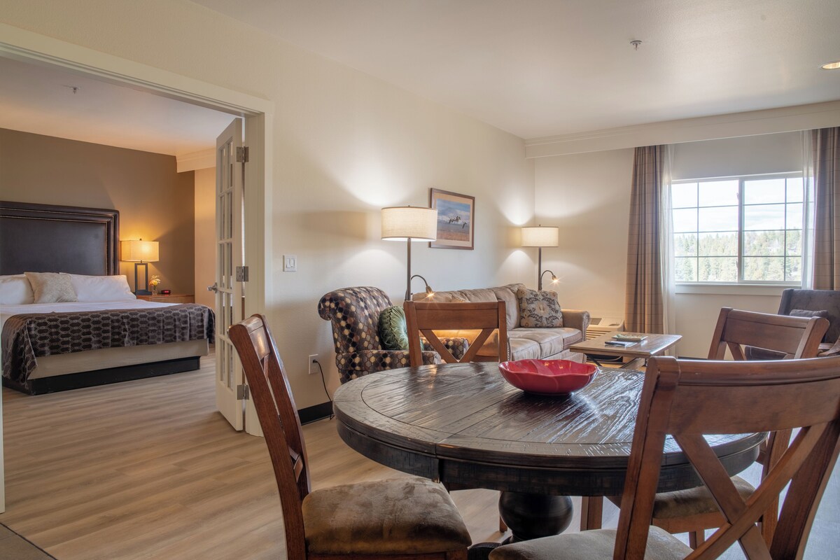 A hotel room with a bed, a dining table with chairs, a sofa, and a window with curtains.