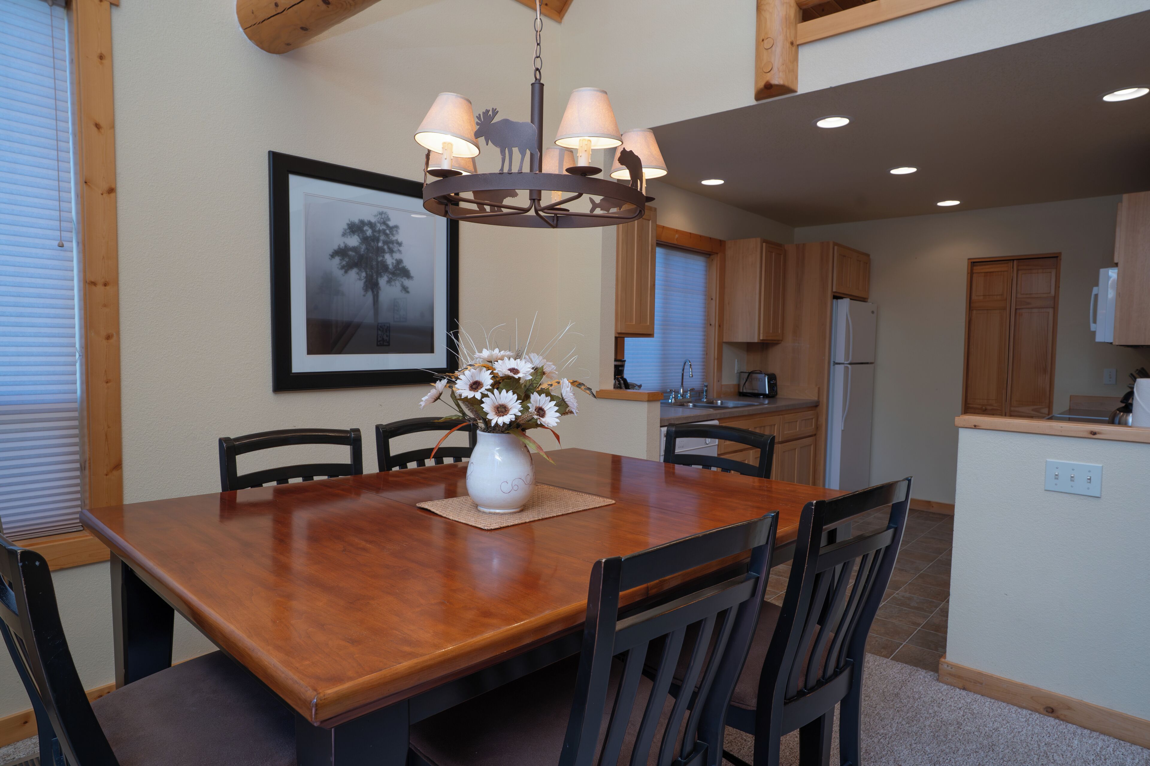 A dining area with a wooden table, chairs, a vase with flowers, and a chandelier.
