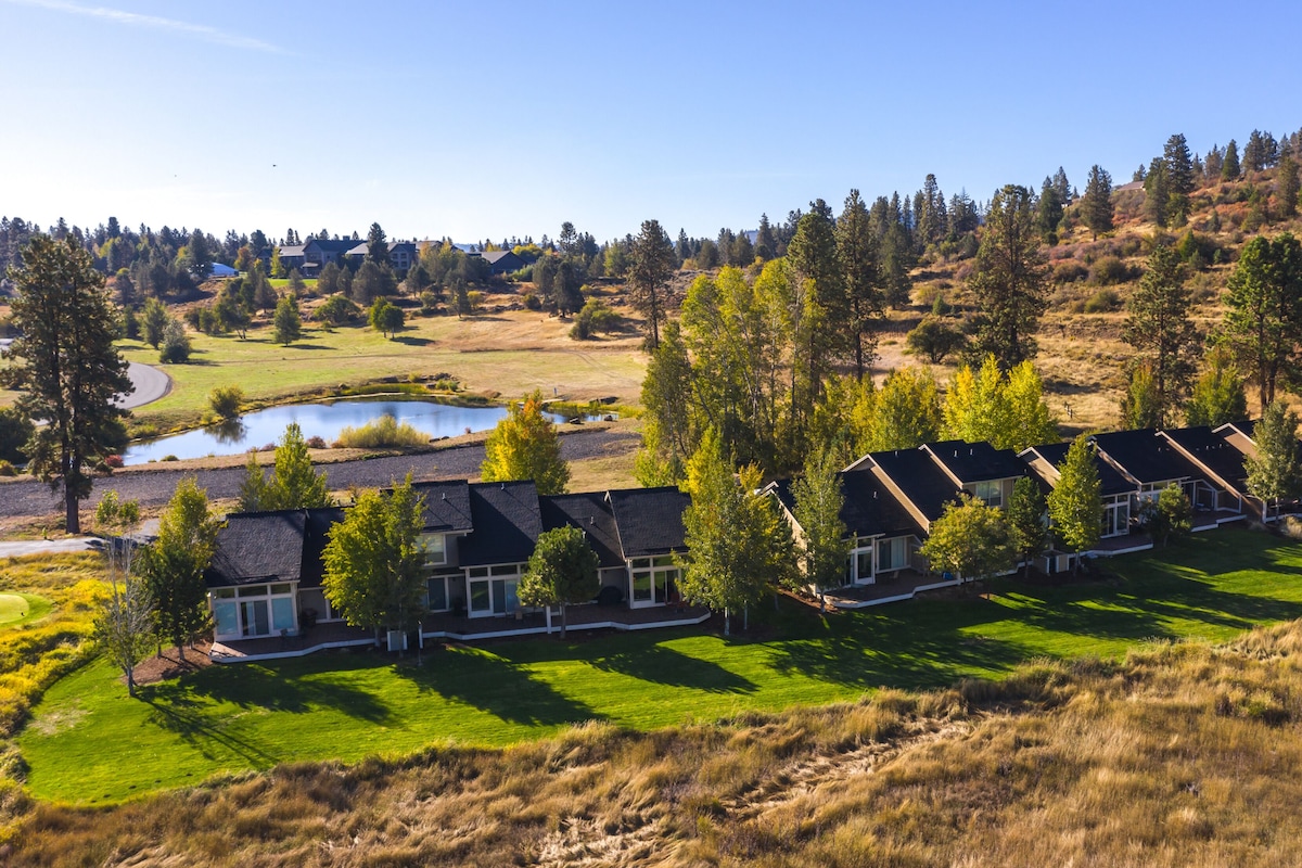 A row of modern houses with a large pond and forested hills in the background.