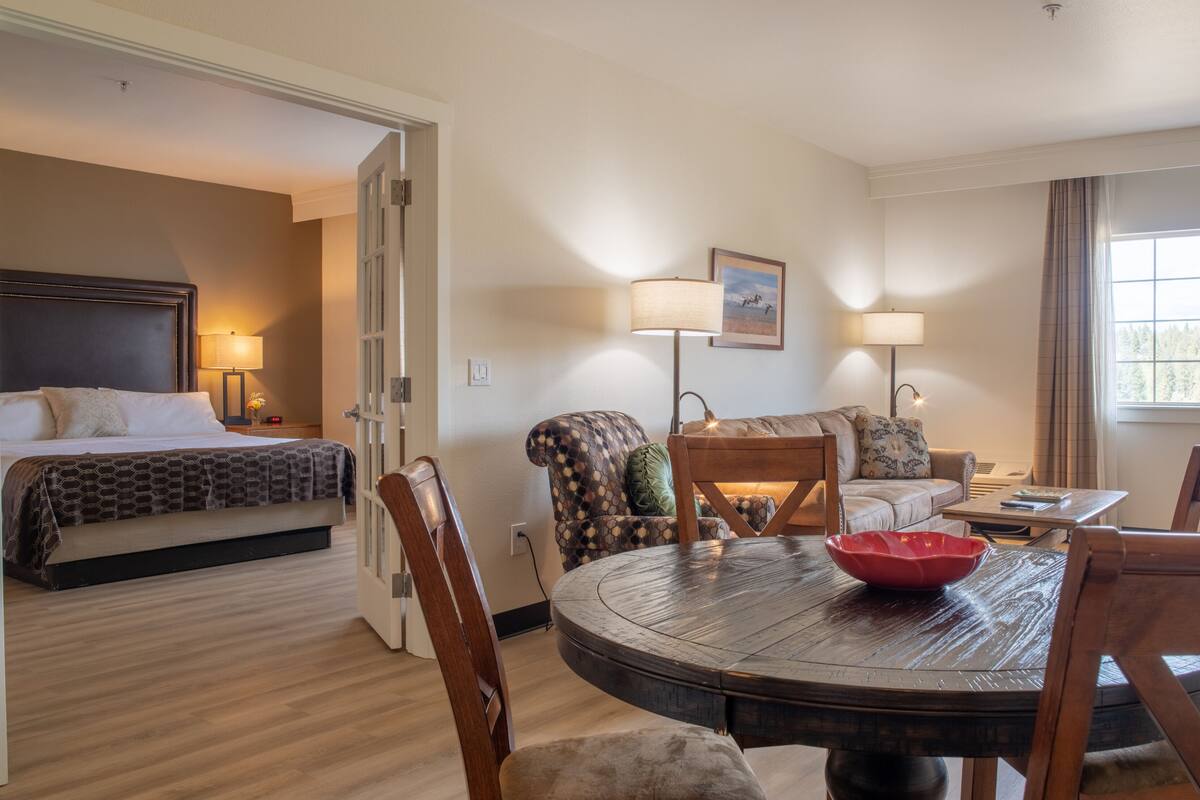 A hotel room with a bed, a sofa, a dining table, and a window.