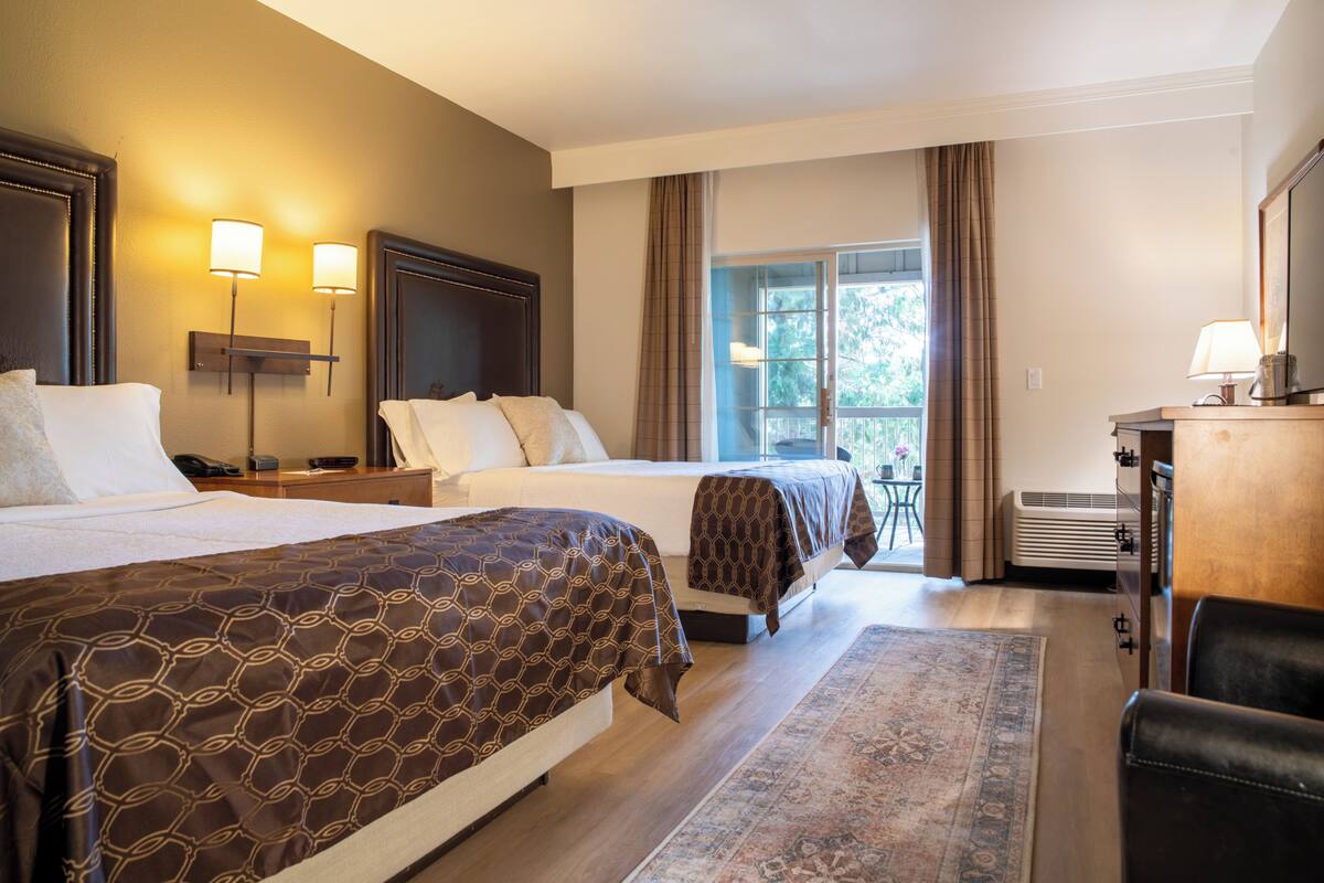 A hotel room with two beds, a desk, a chair, a TV, a lamp, and a window with curtains.