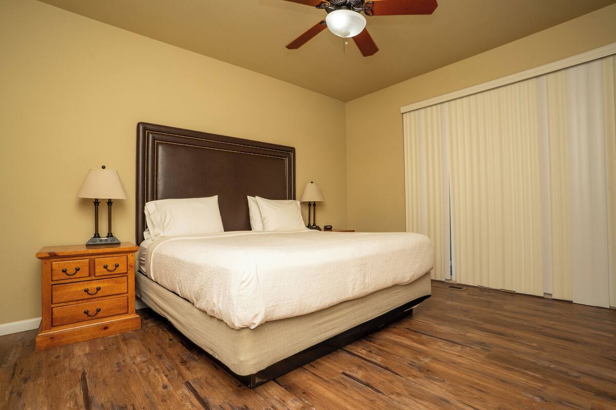 A bedroom with a bed, wooden nightstand, two bedside lamps, a ceiling fan, and a sliding door.