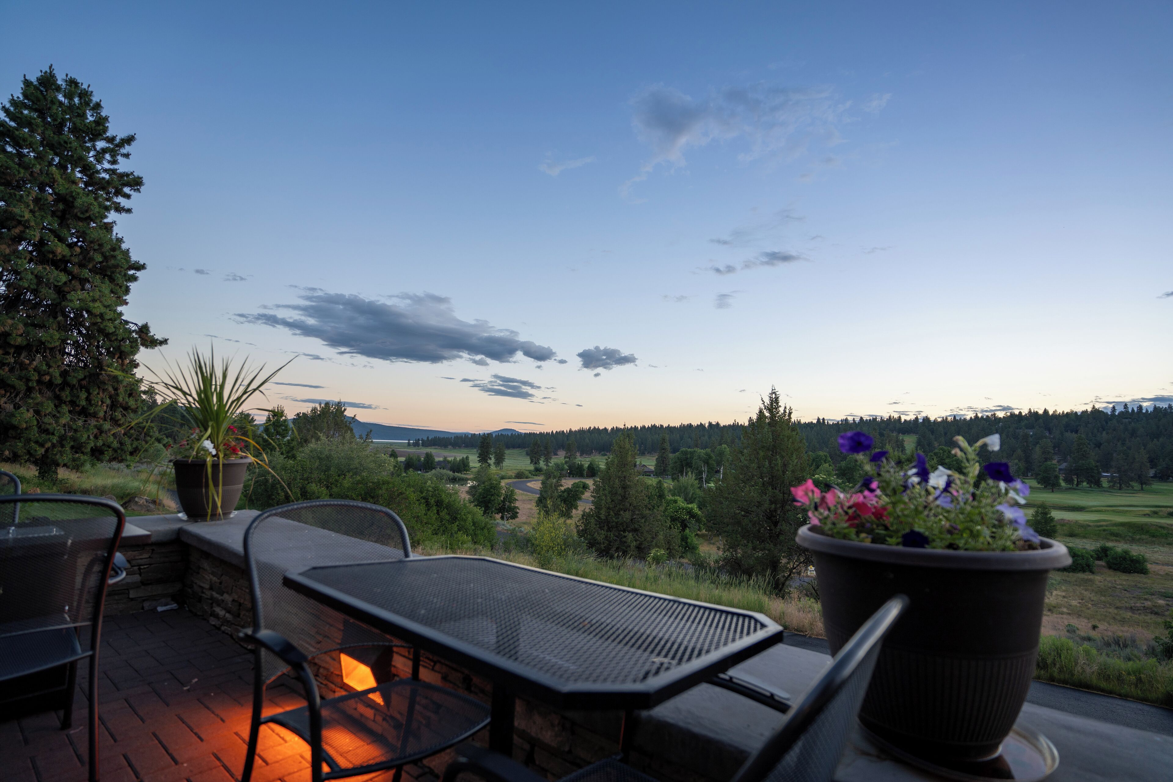 An outdoor patio with a table and chairs, overlooking a scenic landscape with hills and a clear sky.