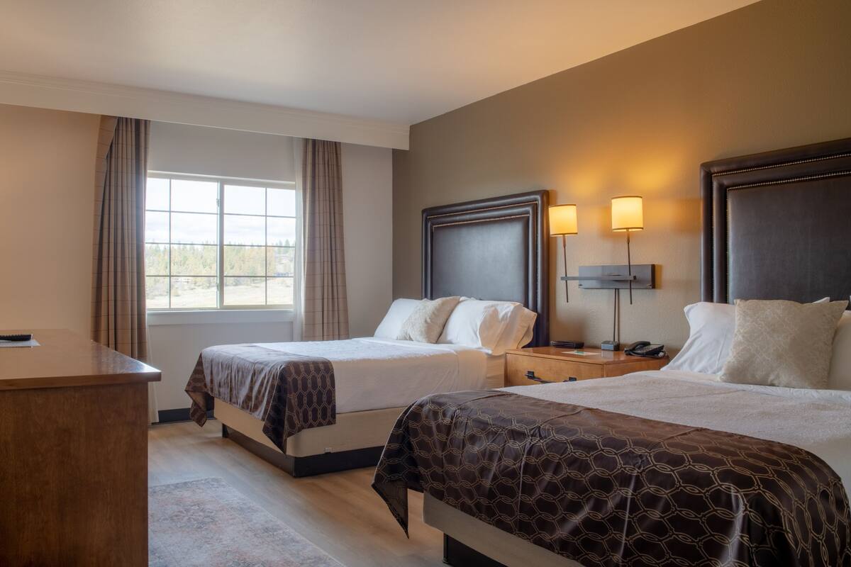 A hotel room with two beds, a desk, a TV, and a window with curtains.
