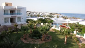 Un bâtiment moderne doté d’un balcon, entouré de jardins bien entretenus et de palmiers, et offrant une vue sur la côte.