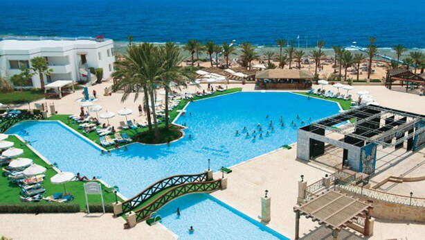 Un complexe hôtelier doté d’une grande piscine centrale, d’un espace de plage avec des chaises longues et d’une scène pour les événements.