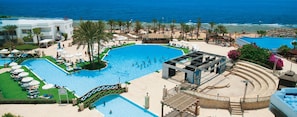 Resort com uma ampla piscina central, área de praia com espreguiçadeiras e palco para eventos.
