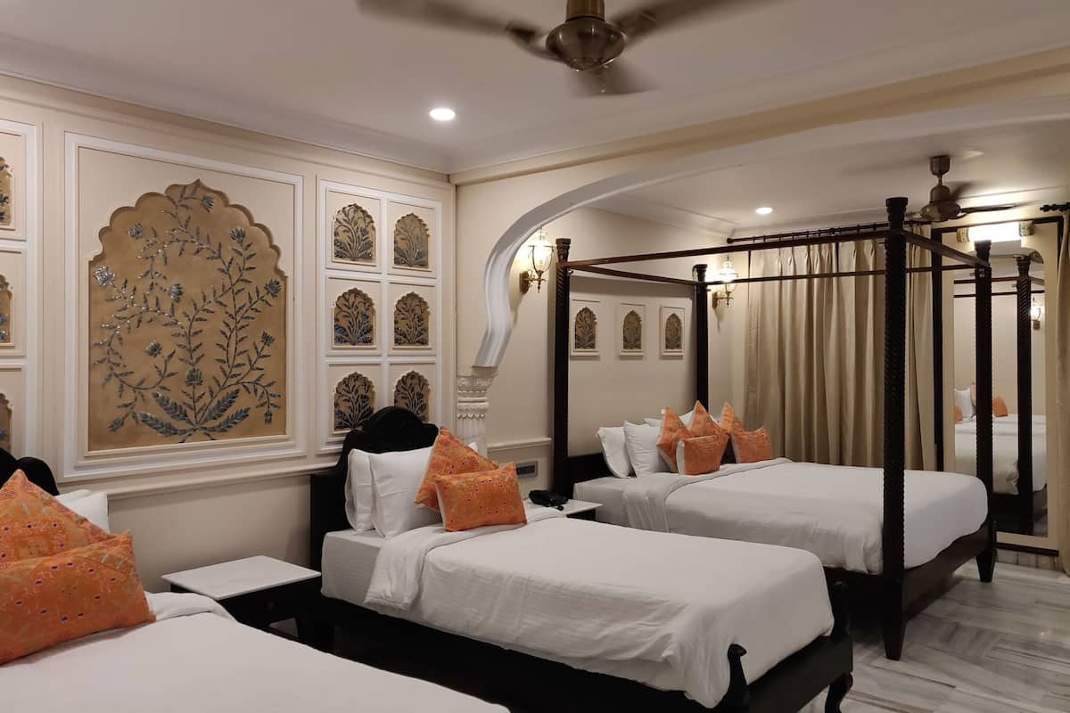 A hotel room with two beds, a canopy bed, decorative wall panels, and a ceiling fan.