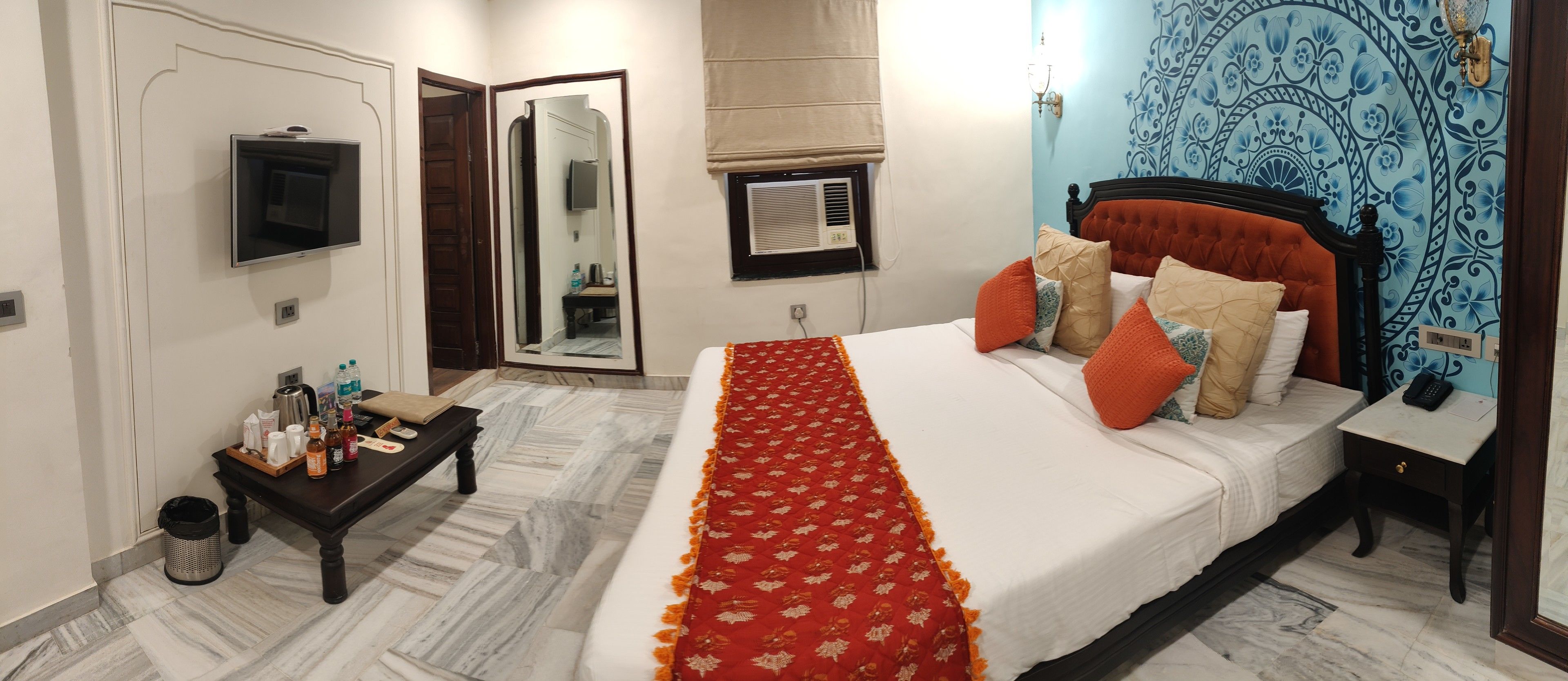 Habitación de hotel con cama, mesita de noche, espejo, equipo de aire acondicionado y una pared con diseño decorativo.