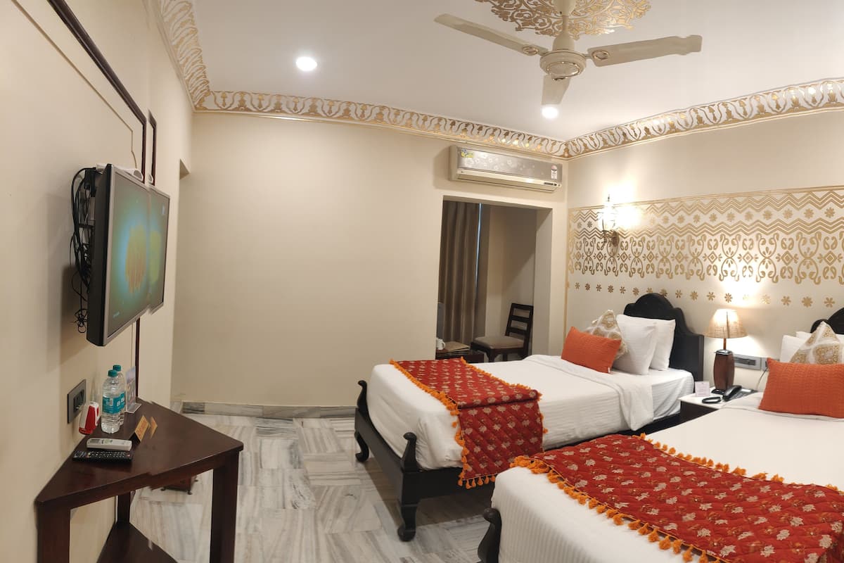 Una habitación de hotel con dos camas, televisión, escritorio y aire acondicionado.