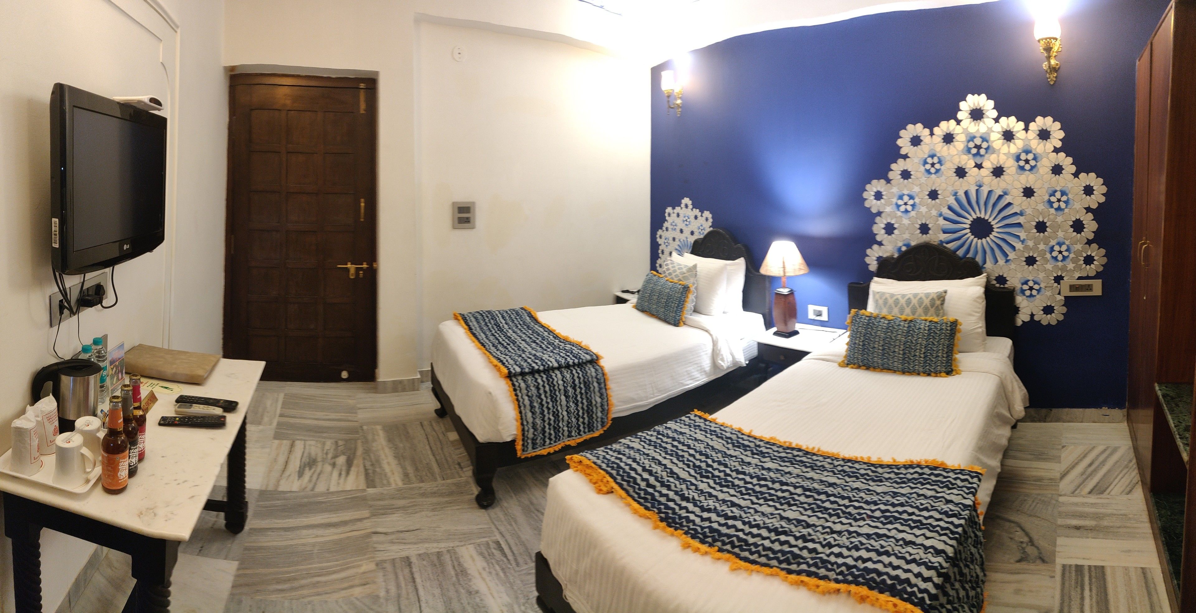 A hotel room with two beds, a TV, a table with drinks, and a decorative wall.