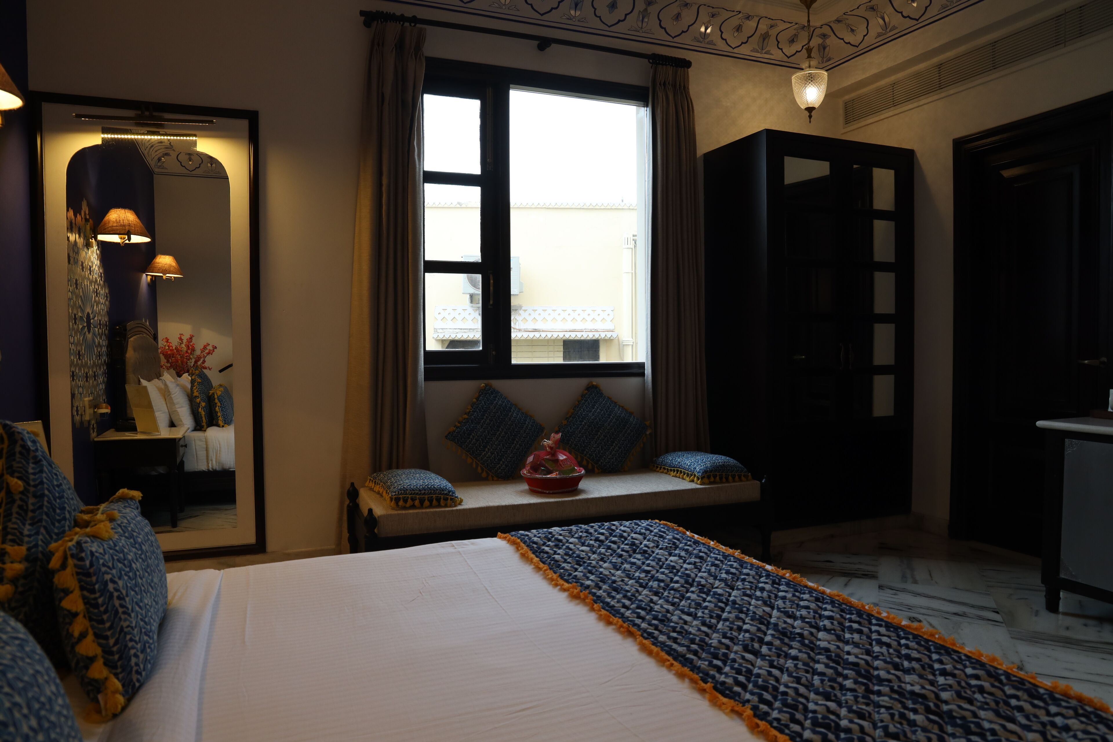 A hotel room with a bed, a window with curtains, a bedside table with a lamp, and a mirror.