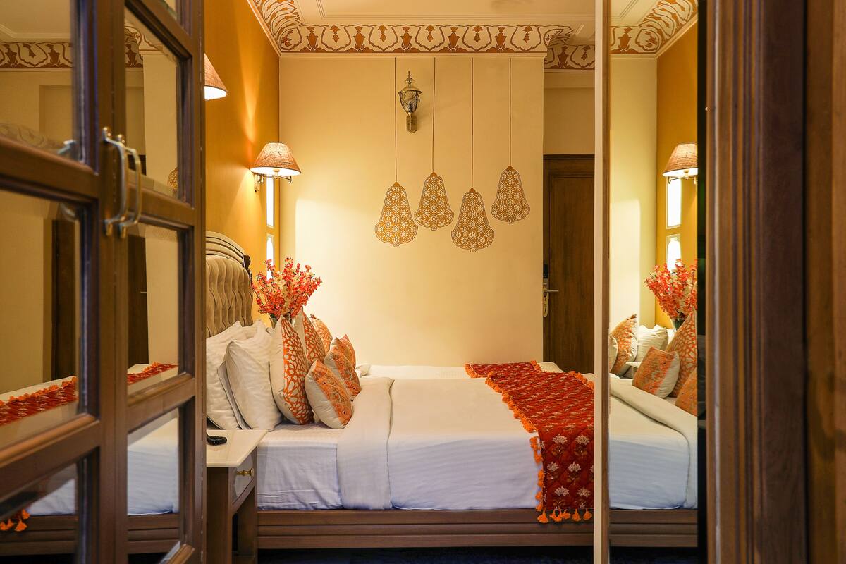 Habitación de hotel con cama, mesita de noche, espejo y lámpara de pared.