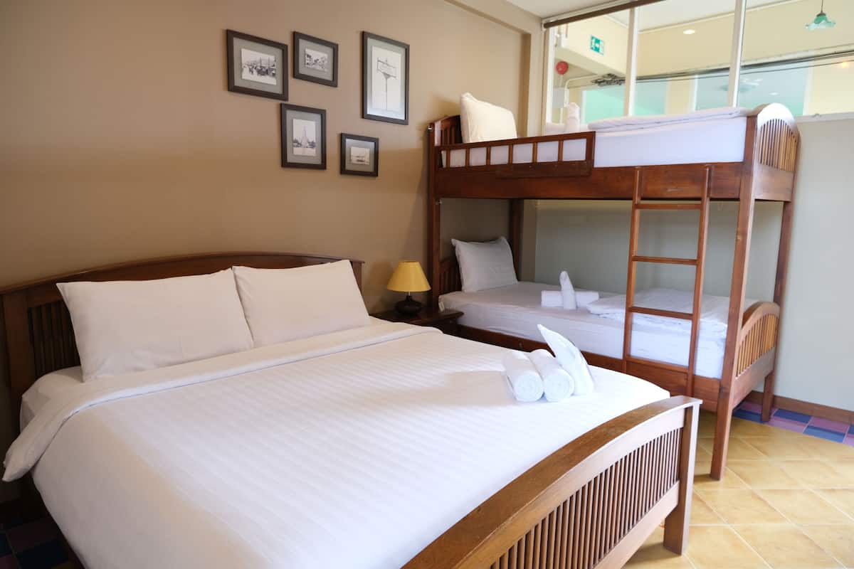 A hotel room with a large bed, a smaller bed, and a bunk bed. There are framed pictures on the wall and a window with a view.