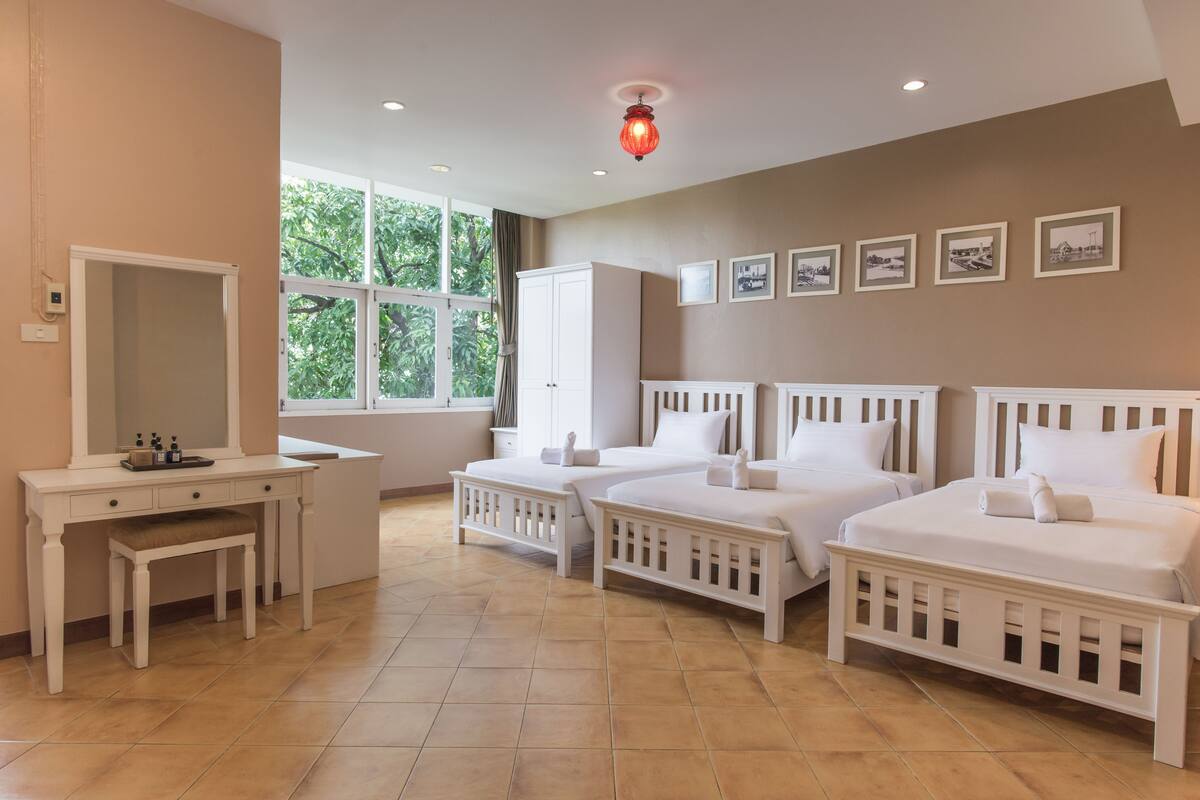 A hotel room with two beds, a vanity with a mirror, and a window with a view of trees.