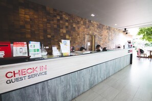 A hotel reception area with a 'Check In Guest Service' sign, a wooden wall, and a counter with various informational posters. - Feung Nakorn Balcony Rooms and Cafe (Bangkok)