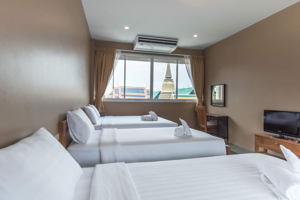A hotel room with two beds, a television, and a window with a view of a temple.