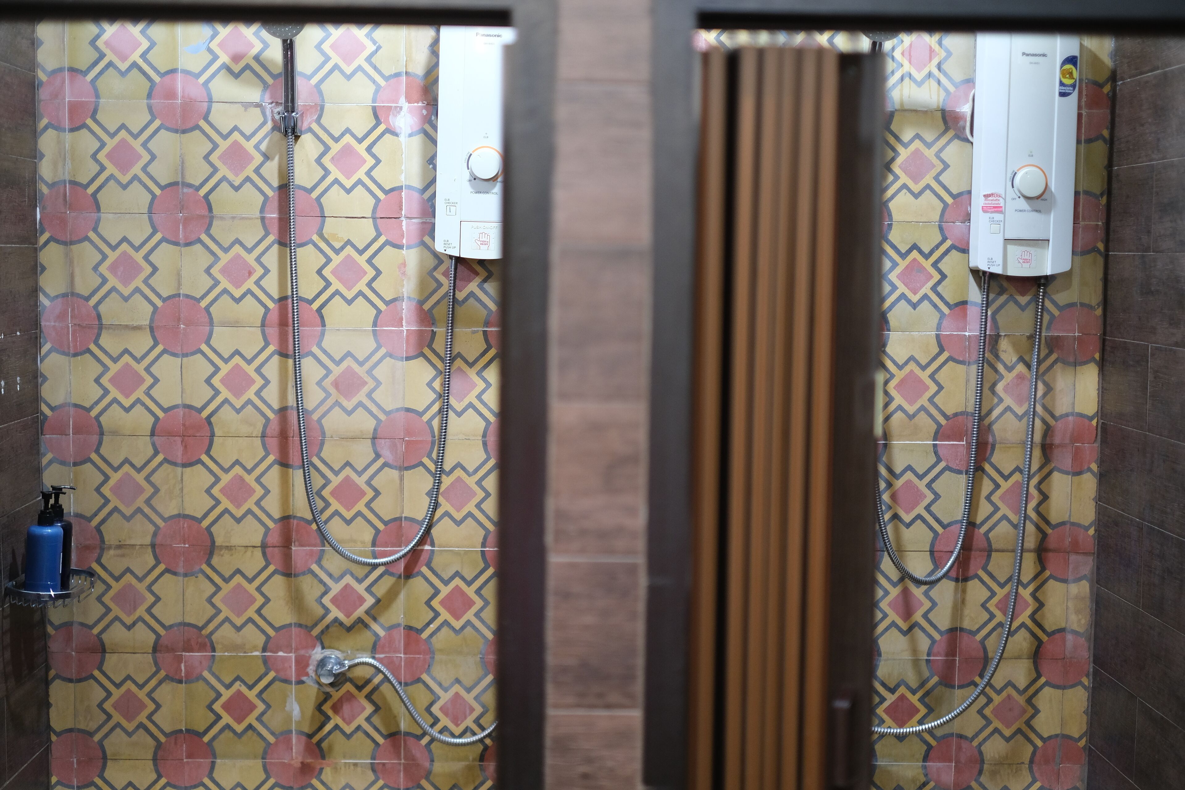 A bathroom with patterned tiles, a shower, and a hand sanitizer dispenser.