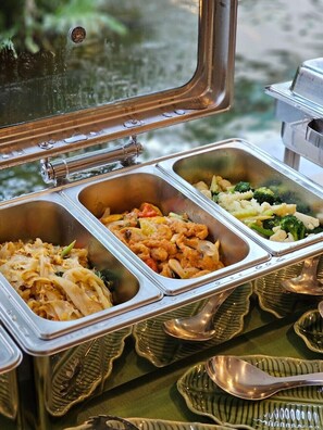 Un bufé con varios recipientes de comida, entre ellos fideos, verduras salteadas y pasta.