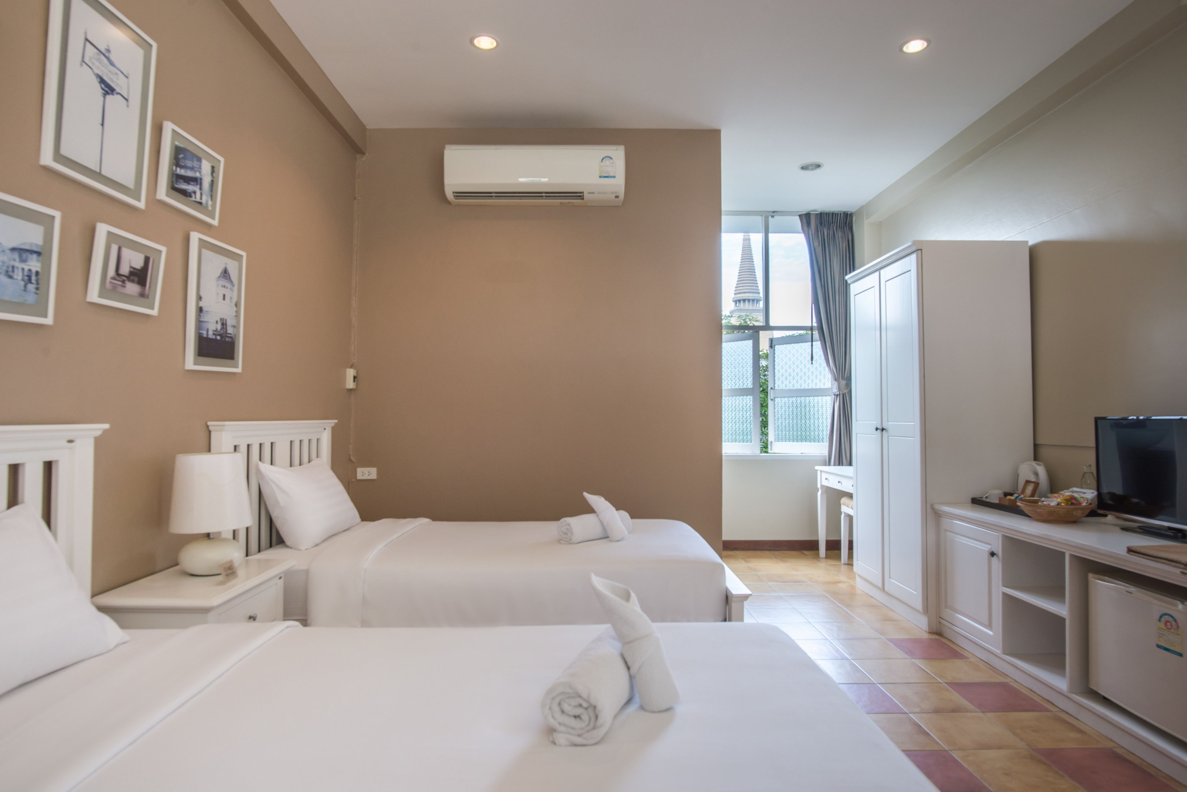 A hotel room with two beds, a TV, a desk, and a window with curtains.
