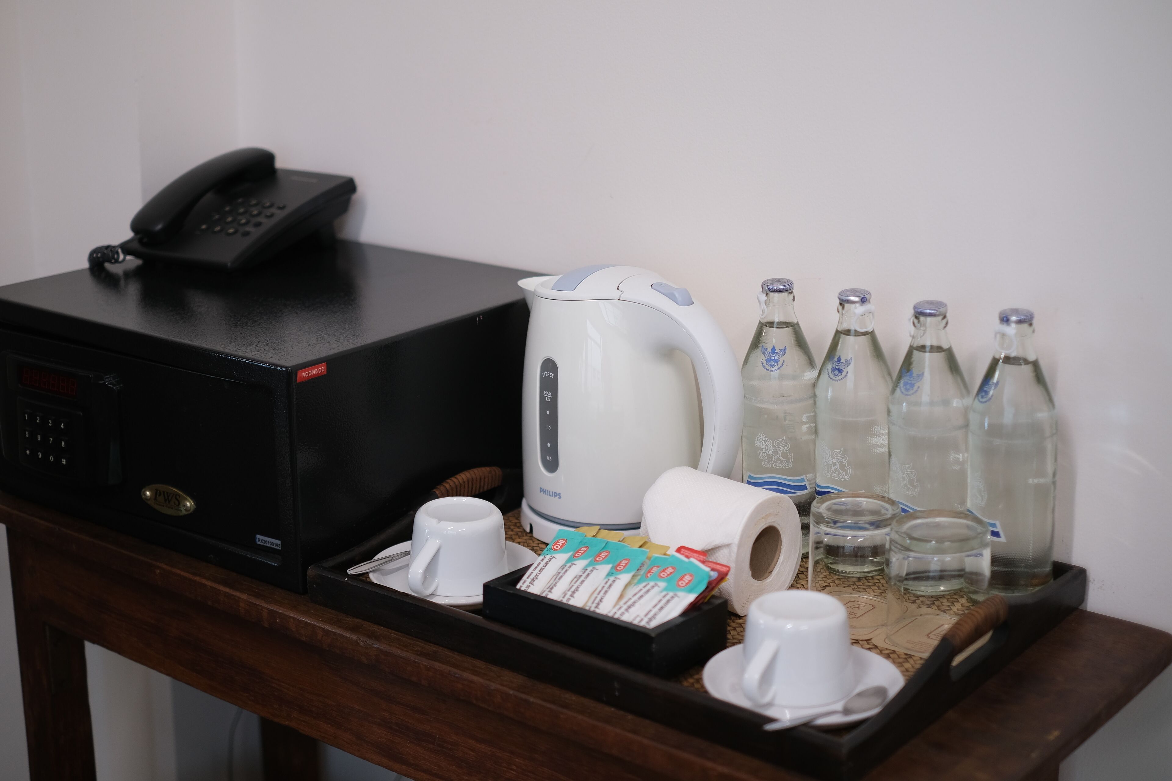 A hotel room's minibar with a coffee maker, tea packets, bottled water, and a telephone.