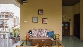 A balcony with a wooden table and chairs, a sofa with patterned cushions, and a view of a building with scaffolding.