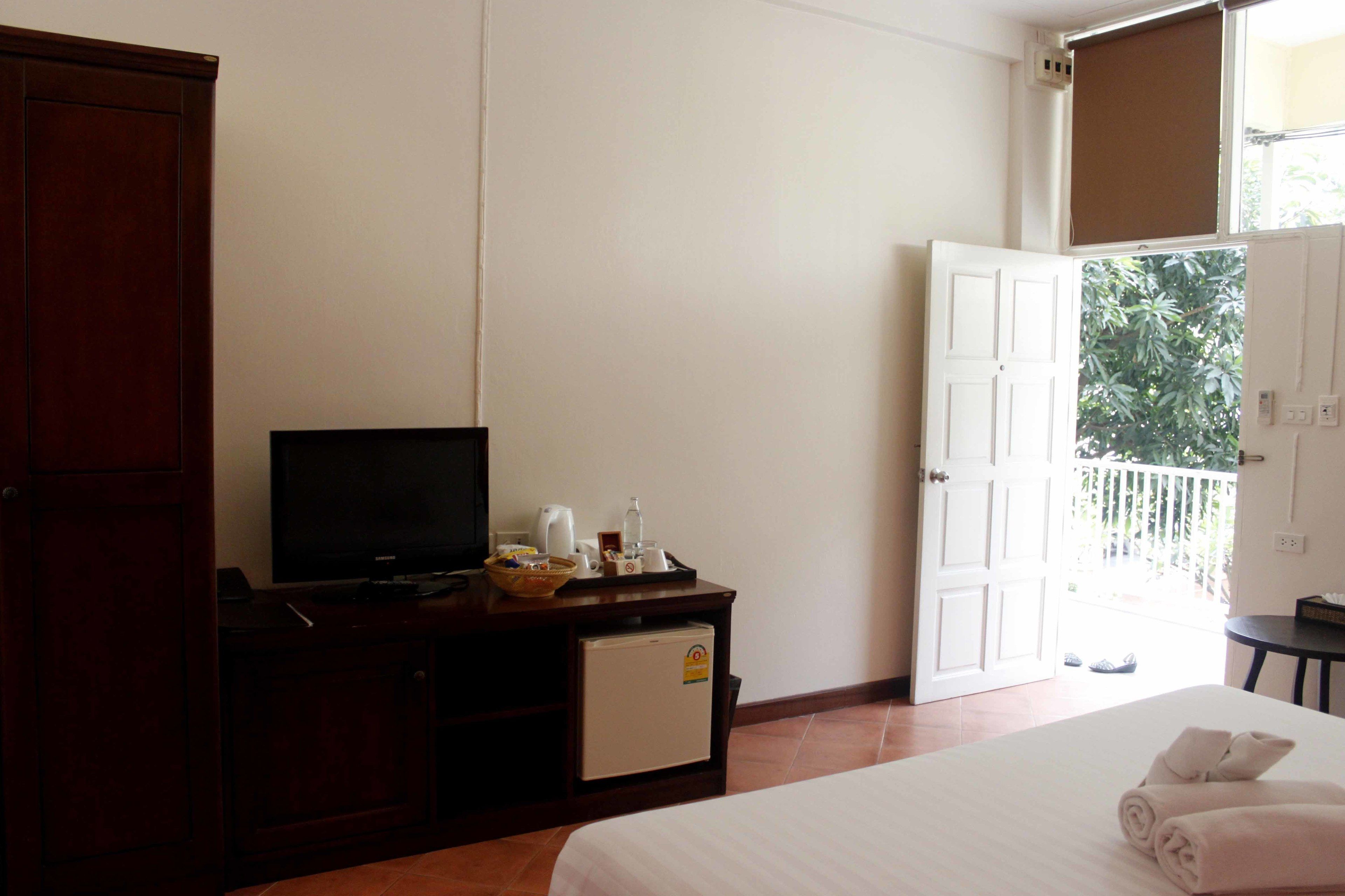 Een hotelkamer met een bed, een televisie op een houten kast, een kleine koelkast, en een balkon met uitzicht op groen.