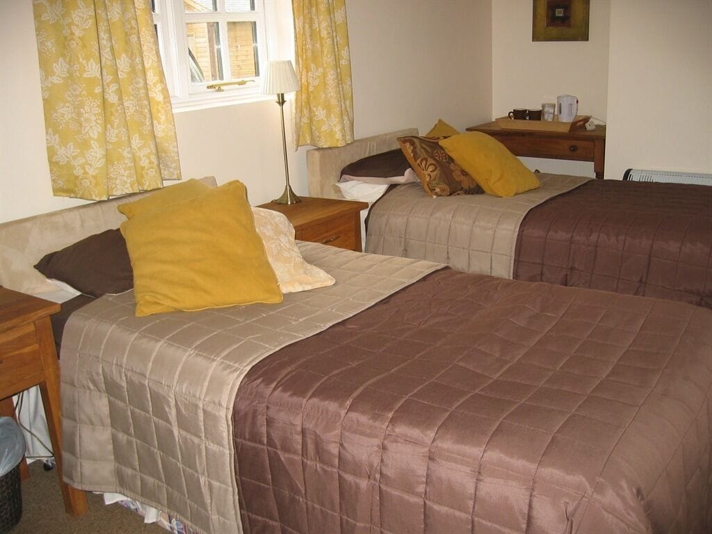 A room with two beds, each with a different colored bedspread, a nightstand, a lamp, and a window with curtains.