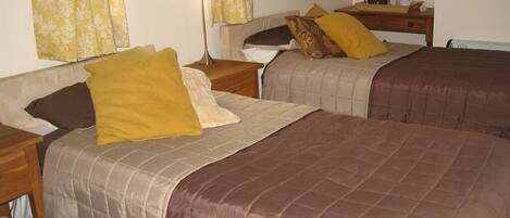 A room with two beds, each with a different colored bedspread, a nightstand, a lamp, and a window with curtains.