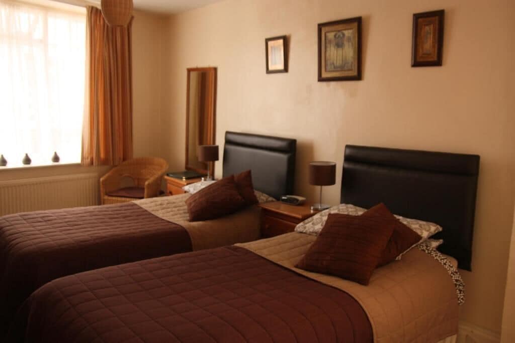 Habitación de hotel con dos camas, una silla, un escritorio y una ventana con cortinas.