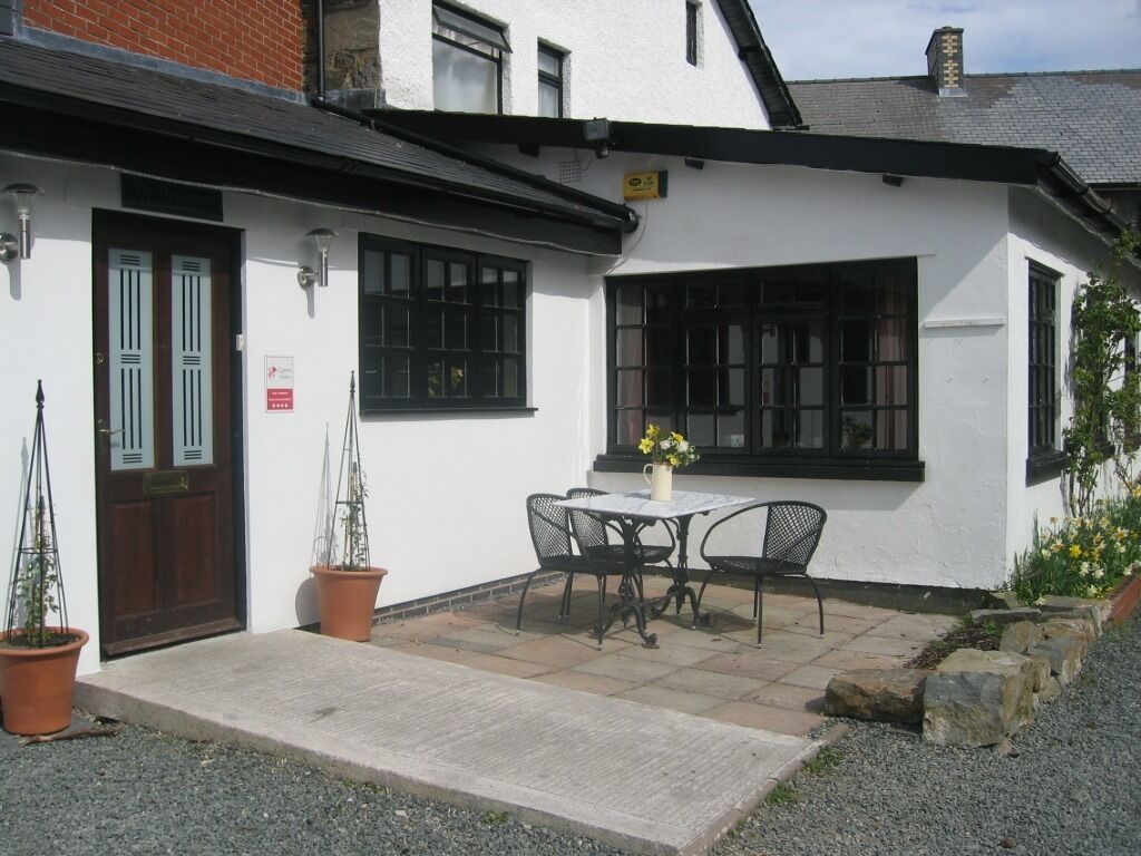 A white building with a black door, a window, and a small table with chairs outside.