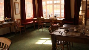 A dining area with a wooden table and chairs, a window with curtains, and a green carpeted floor.