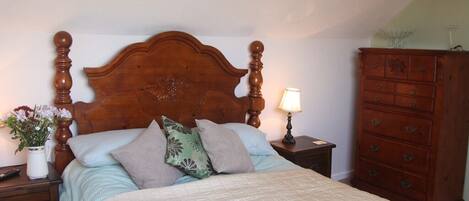 Un dormitorio con cabecera de cama de madera, una mesita de noche con lámpara, un aparador y un florero con flores.