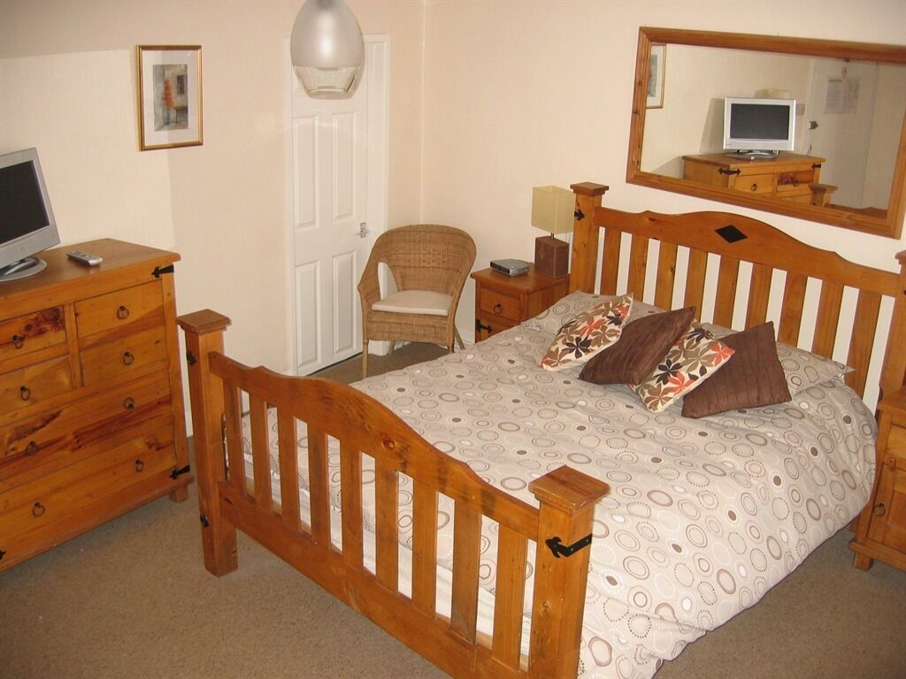 Une chambre à coucher avec un lit en bois, une commode, une chaise, une table de chevet, une lampe, un téléviseur et un miroir.