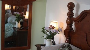 A bedroom with a wooden headboard, a bedside table with a lamp, a mirror, and a vase with flowers.