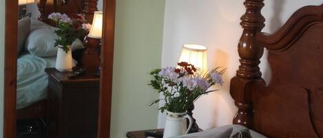 A bedroom with a wooden headboard, a bedside table with a lamp, a mirror, and a vase with flowers.