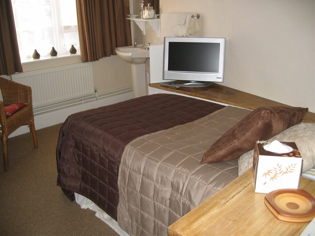 A bedroom with a bed, a television on a wooden table, a chair, and a window with curtains.