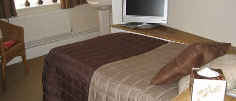 A bedroom with a bed, a television on a wooden table, a chair, and a window with curtains.