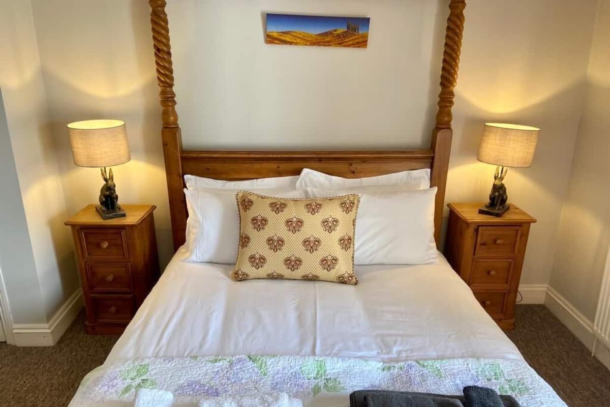 Un lit bien fait, avec du linge de lit blanc, un coussin à motifs et deux lampes de chevet posées sur des tables de nuit en bois.