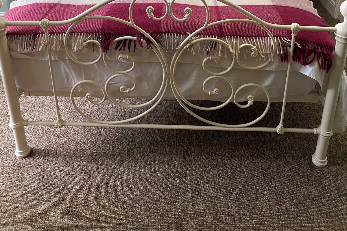Un lit bien fait, avec une structure en métal, une literie blanche et des coussins décoratifs. Deux tables de chevet, sur lesquelles sont posées des lanternes, se trouvent de chaque côté du lit.