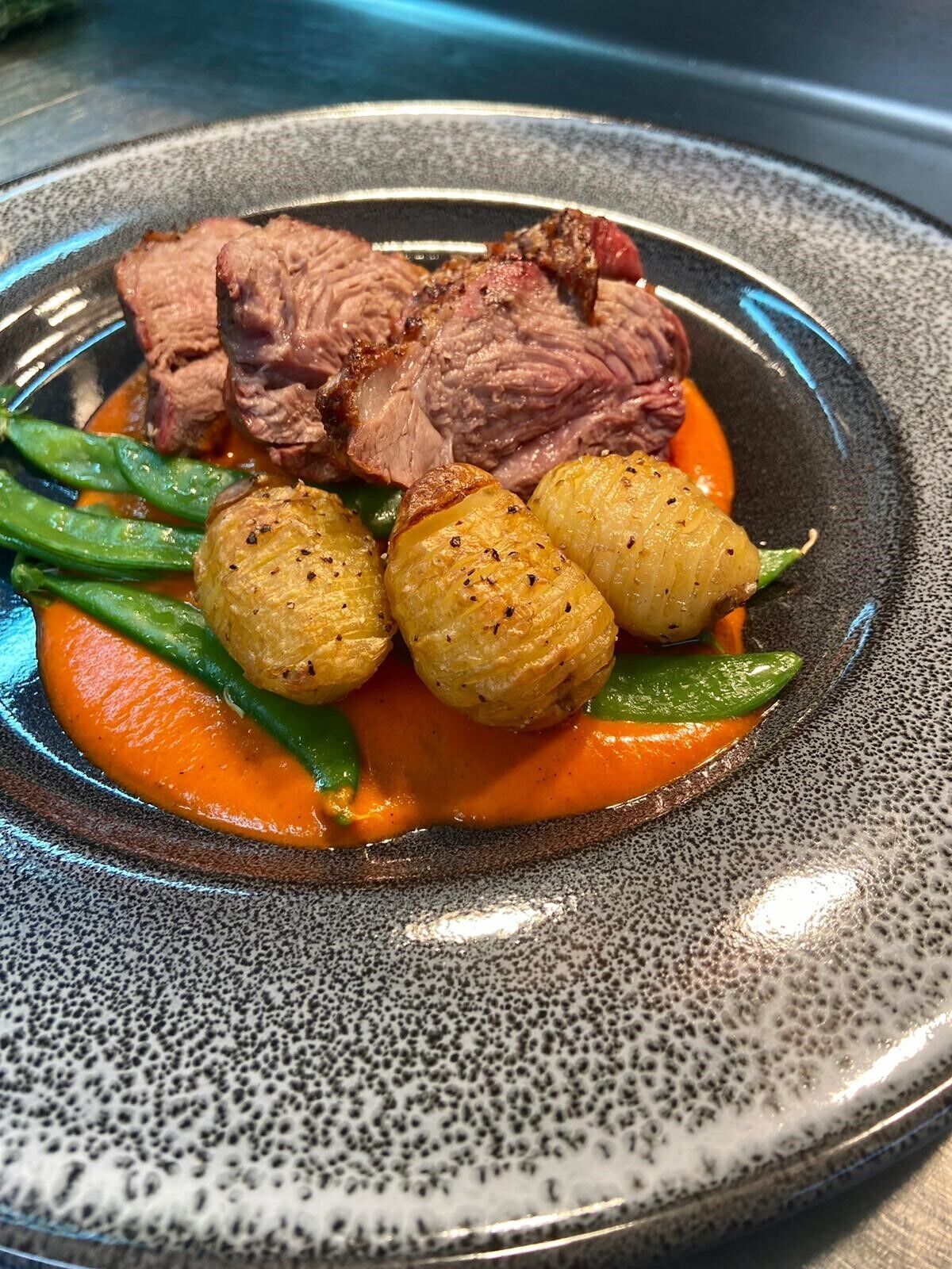 Un plato de comida con carne en rodajas, patatas asadas y verduras verdes.