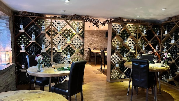 Ein Restaurant mit Holztischen und -stühlen, einer Ziegelwand und einem Weinkühlschrank mit Flaschen.