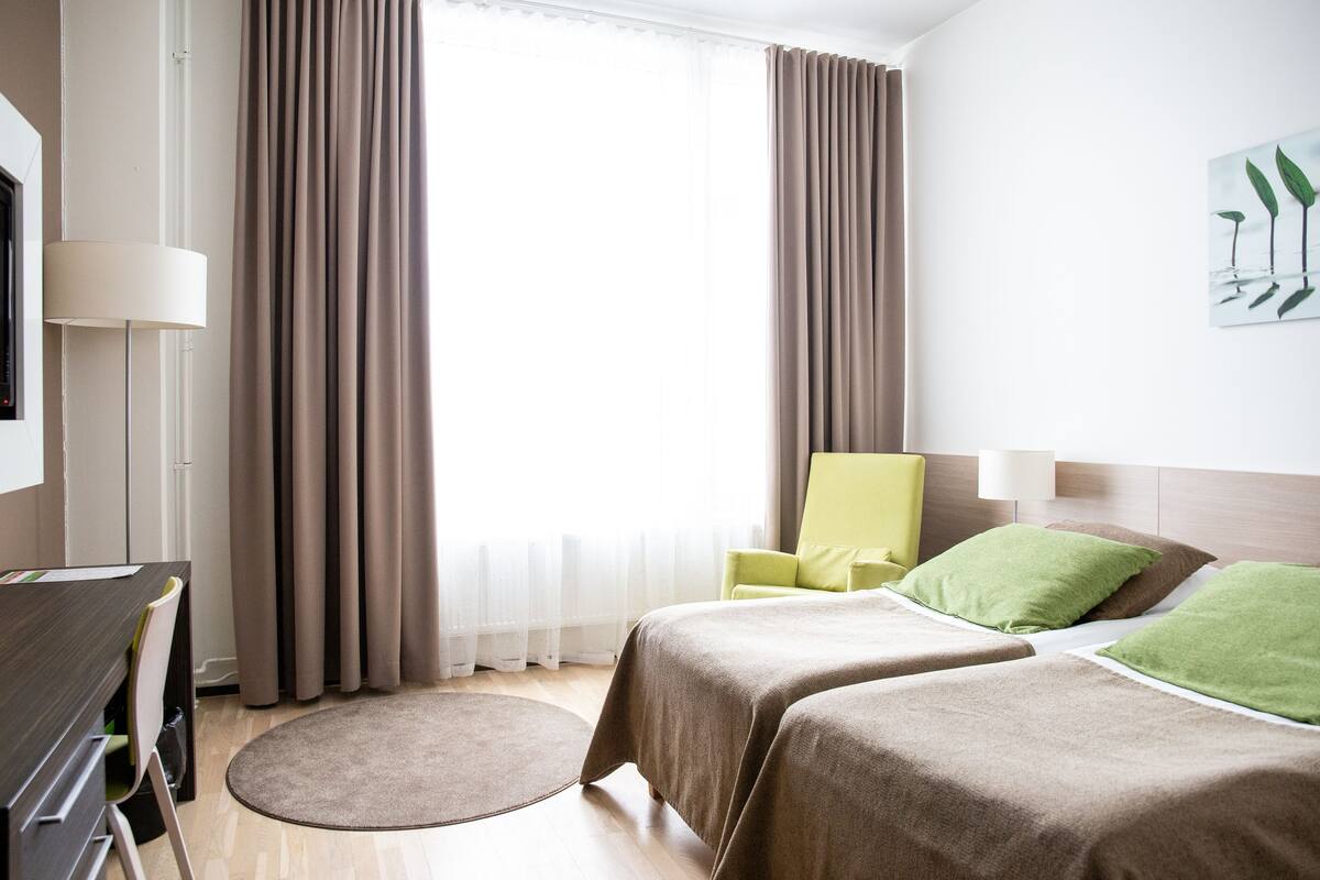 Une chambre d’hôtel avec un lit, une chaise, un bureau et une fenêtre avec des rideaux.