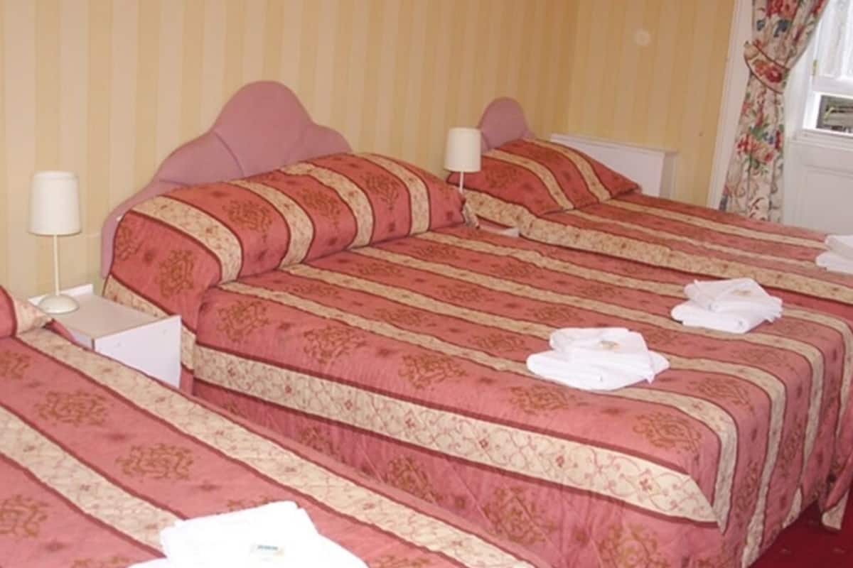A hotel room with two beds, each with a red and beige patterned bedspread, white pillows, and a white nightstand with a lamp.