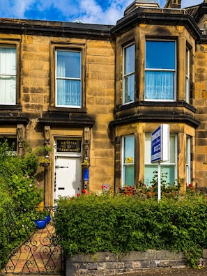 A corner building with a white door, a blue sign, and a window with a curtain. - Menzies Guest House (Edinburgh)