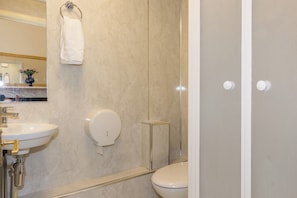 A bathroom with a marble wall, a white sink, a toilet, and a glass shower enclosure. - Menzies Guest House (Edinburgh)