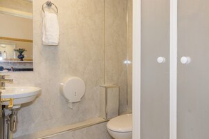 Ein Badezimmer mit Marmorwand, einem weißen Waschbecken, einer Toilette und einer Duschkabine aus Glas.